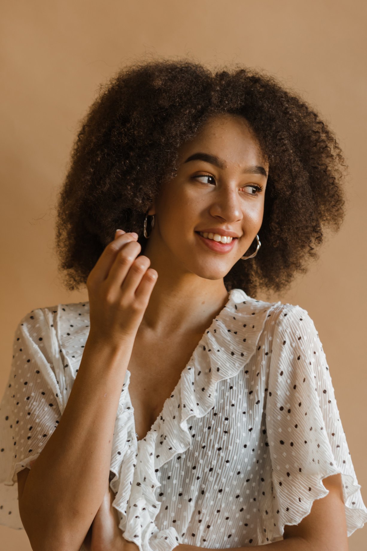 Smiling young ethnic woman looking away in beige studio